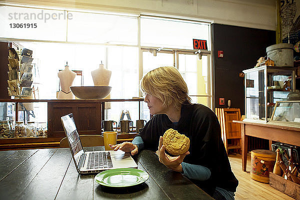 Frau benutzt Laptop  während sie im Café am Tisch sitzt