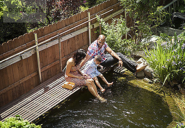 Hochwinkelaufnahme einer Familie  die auf einem Fußweg über einem Teich im Hinterhof sitzt