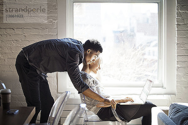 Seitenansicht des Paares mit Laptop am Fenster zu Hause