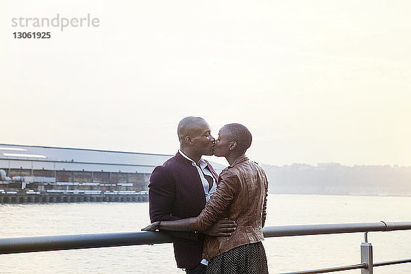 Zärtliches Paar  das sich küsst  während es am Pier am Geländer steht