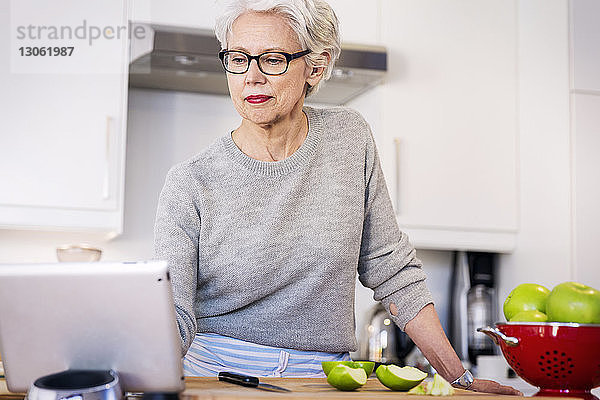 Ältere Frau betrachtet Rezept auf digitalem Tablett  während sie in der Küche steht