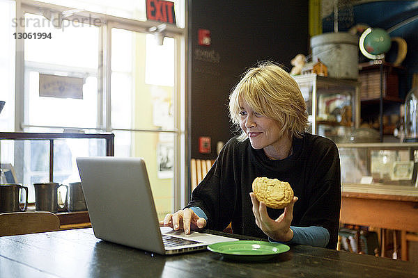 Glückliche Frau benutzt Laptop  während sie im Café am Tisch sitzt