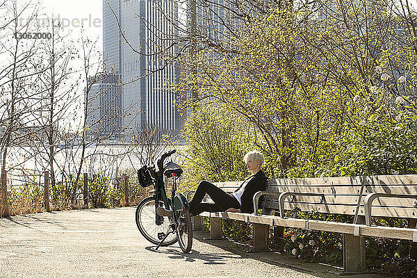 Frau ruht auf Bank neben geparktem Fahrrad am Fluss in der Stadt