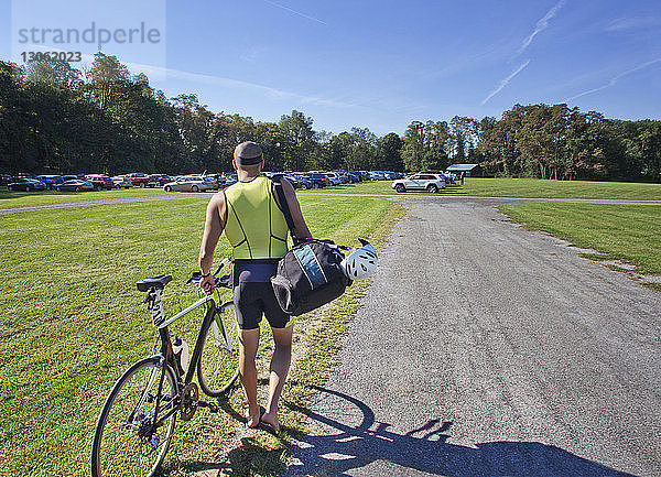 Rückansicht eines Mannes zu Fuß mit Fahrrad auf dem Feld