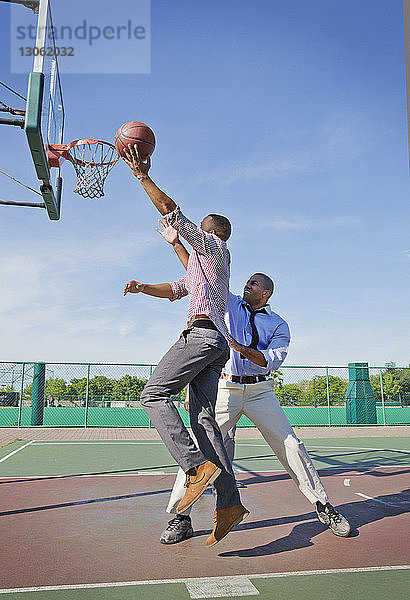 Männer spielen an sonnigen Tagen Basketball auf dem Platz