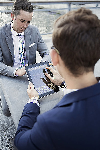 Geschäftsmann benutzt digitales Tablett  während er mit seinem Kollegen am Tisch sitzt