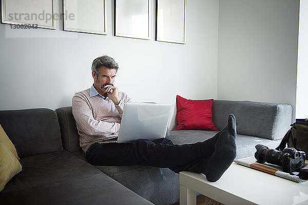 Seriöser Geschäftsmann benutzt Laptop  während er im Hotelzimmer auf dem Sofa sitzt