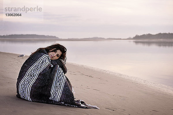 Bildnis einer in eine Decke gehüllten Frau am Strand sitzend