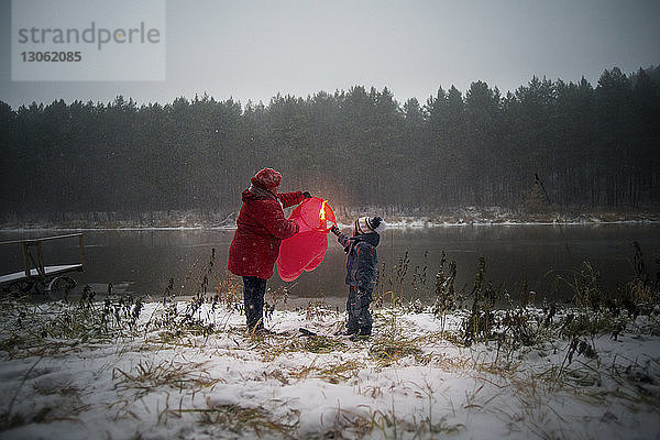Grossmutter und Sohn halten Papierlaterne auf schneebedecktem Feld