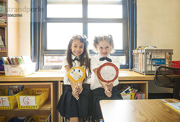 Porträt glücklicher Schulmädchen  die im Klassenzimmer stehend handwerkliche Produkte halten