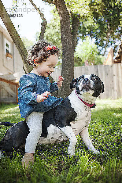 Glückliches kleines Mädchen sitzt auf Hund im Garten