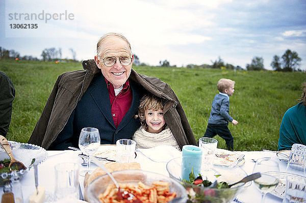 Porträt eines glücklichen Mädchens  das mit dem Großvater am Tisch auf dem Feld sitzt