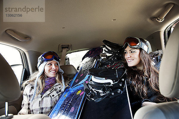 Glückliche Skifahrerinnen sitzen im Auto an Snowboards