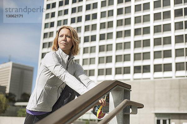 Frau schaut weg  während sie sich am Geländer gegen Gebäude in der Stadt streckt