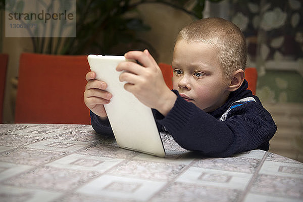 Junge benutzt Tablet-Computer  während er am Tisch sitzt