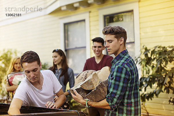 Mann hält Brennholz  während er vor dem Haus bei Freunden steht