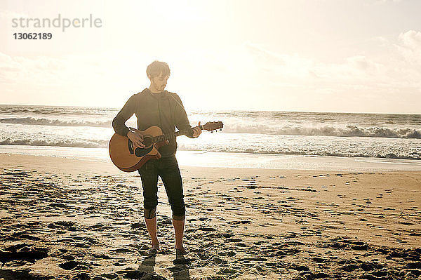 Mann spielt Gitarre  während er am Strand steht