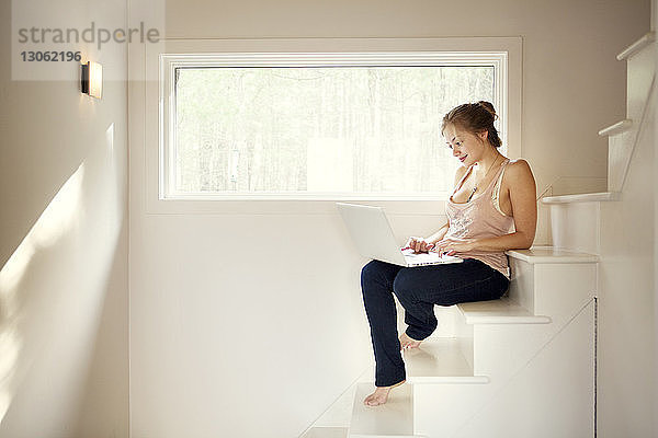 Glückliche Frau  die einen Laptop benutzt  während sie auf einer Treppe sitzt
