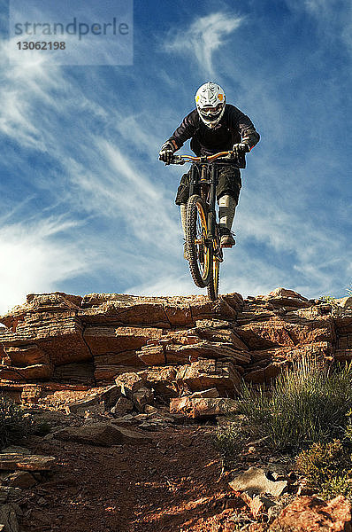 Mountainbiker springen von Klippe gegen Himmel