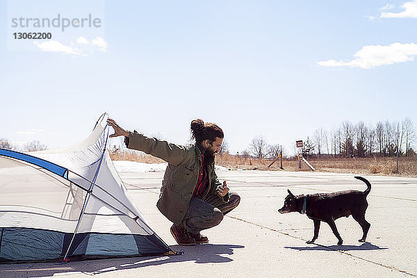 Mann hält Zelt in voller Länge  während er den Hund auf dem Campingplatz betrachtet