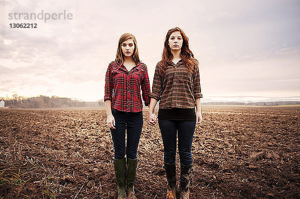 Porträt von Freundinnen  die sich an den Händen halten  während sie auf dem Feld stehen