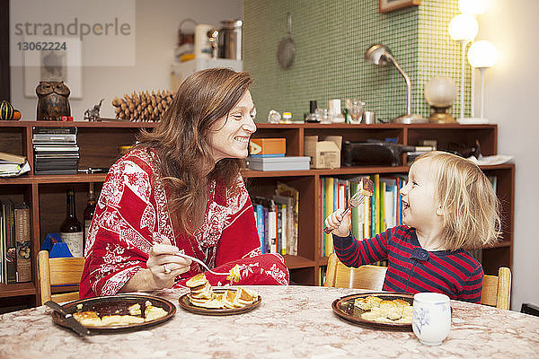 Fröhliche Mutter und Sohn essen Brot bei Tisch