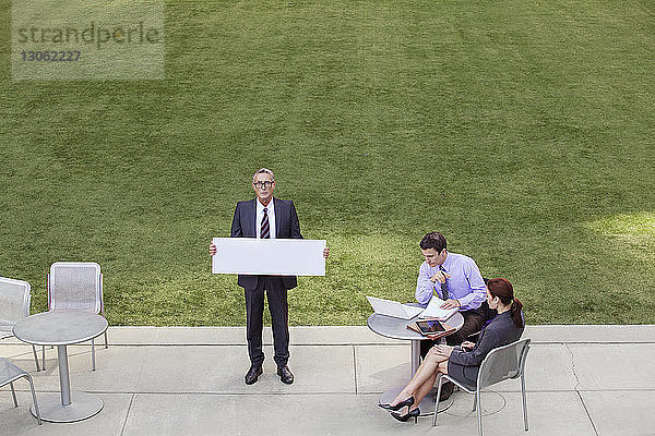 Geschäftsmann hält Diagramm von Kollegen  die am Tisch diskutieren