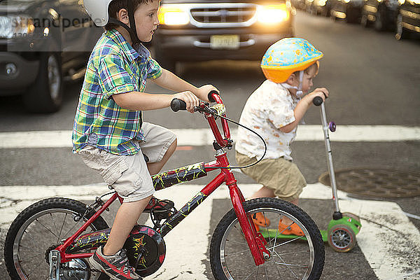 Brüder fahren Roller und Fahrrad auf der Straße
