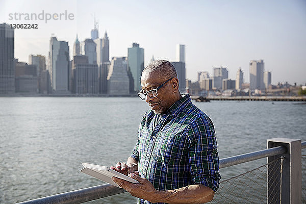 Älterer Mann benutzt Tablet-Computer  während er am East River in der Stadt steht