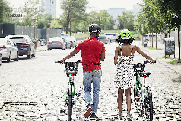 Rückansicht eines Paares mit Fahrrädern  das in der Stadt auf der Straße geht