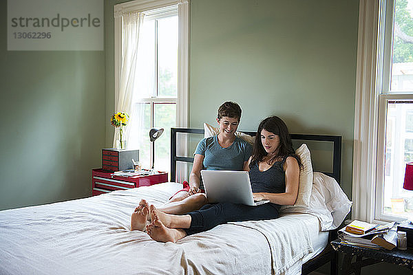 Freundinnen benutzen Laptop  während sie sich zu Hause im Bett entspannen
