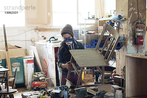 Tischlerin untersucht Holzstuhl in Werkstatt