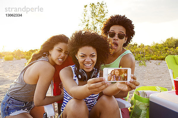 Fröhliche Freunde  die am Strand mit dem Handy telefonieren