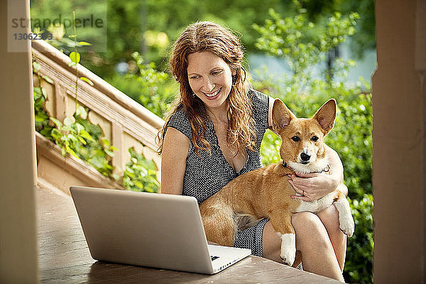 Frau benutzt Laptop-Computer  während sie mit Hund auf der Veranda sitzt