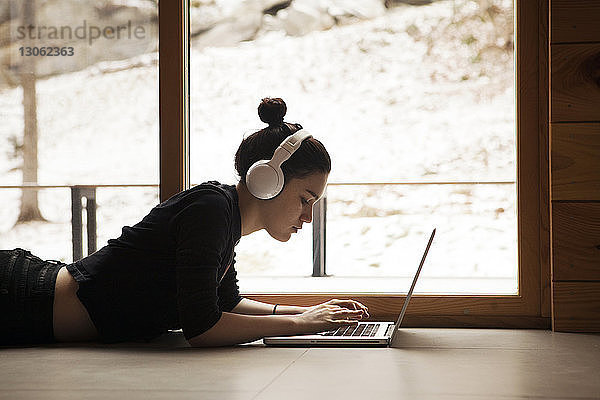 Teenagerin benutzt Laptop  während sie zu Hause auf dem Boden liegt