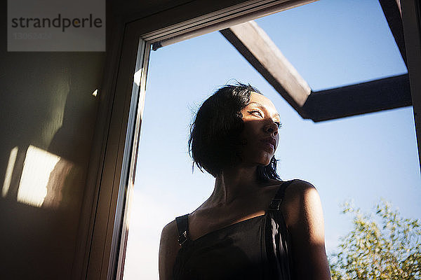 Niedrigwinkelansicht einer Frau  die weg schaut  während sie zu Hause am Fenster steht