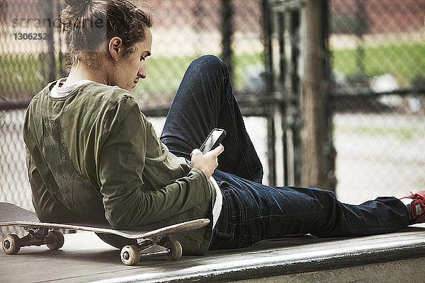 Mann benutzt Smartphone  während er sich auf einem Sitz im Skateboard-Park entspannt