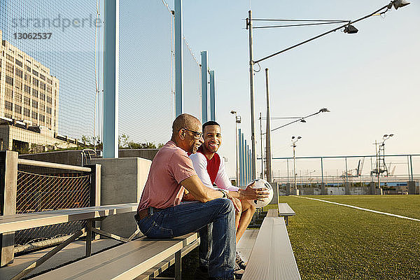 Glückliche Vater und Sohn sitzen auf Tribünen am Fussballplatz