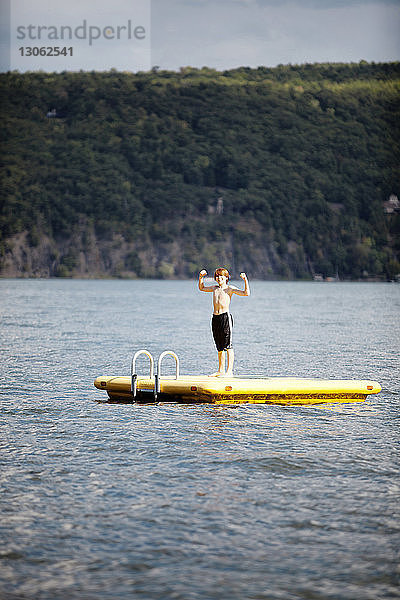 Junge beugt Muskeln  während er auf schwimmender Plattform im See steht