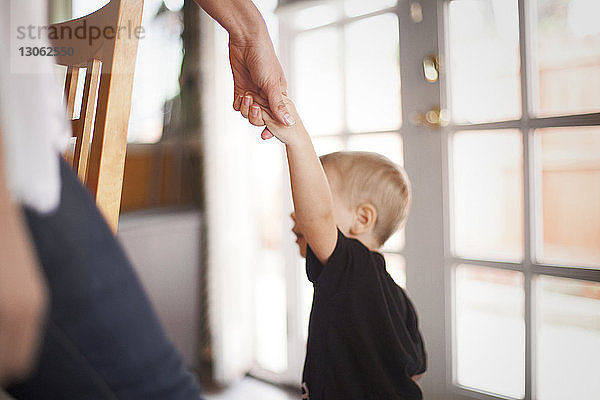 Ausgeschnittenes Bild einer Mutter  die zu Hause die Hand des Sohnes hält