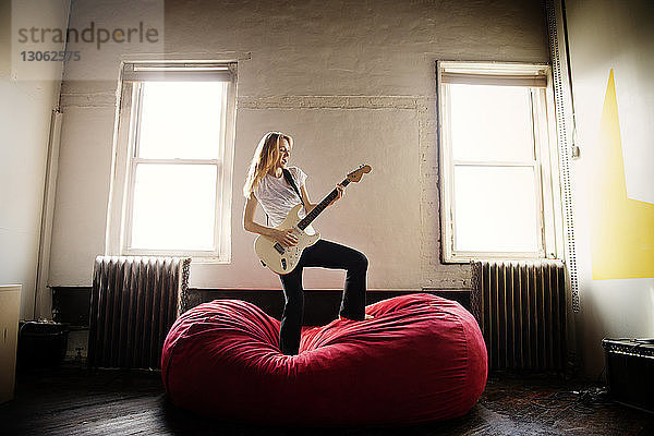 Junge Frau spielt zu Hause E-Gitarre auf Bean Bag