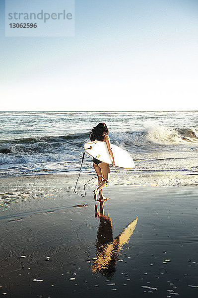 Frau mit Surfbrett beim Strandspaziergang am Ufer