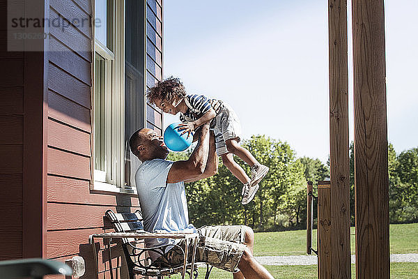 Glücklicher Vater hebt Jungen hoch  während er im Hinterhof sitzt