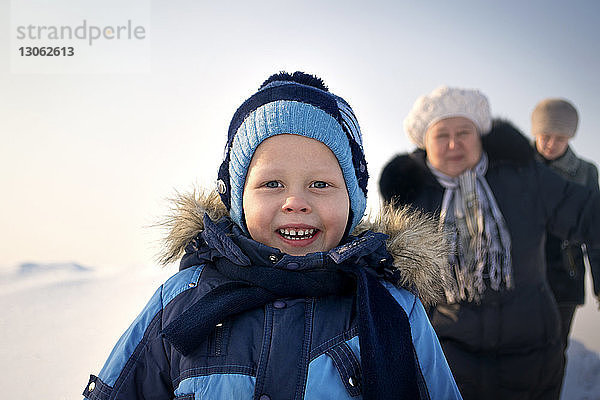 Porträt eines glücklichen Jungen mit Familie  der im Winter auf dem Feld spazieren geht