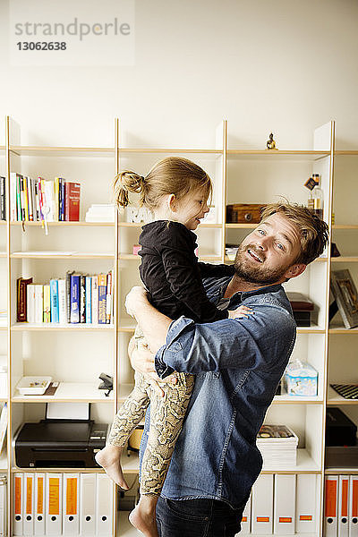 Vater trägt Tochter  während er zu Hause am Regal steht