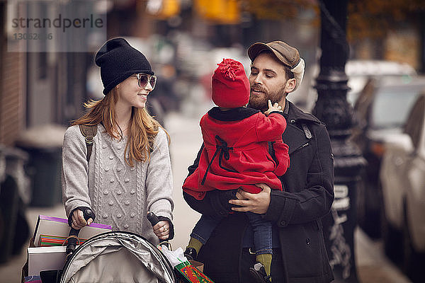 Vater trägt Tochter  während er mit Frau auf der Straße geht