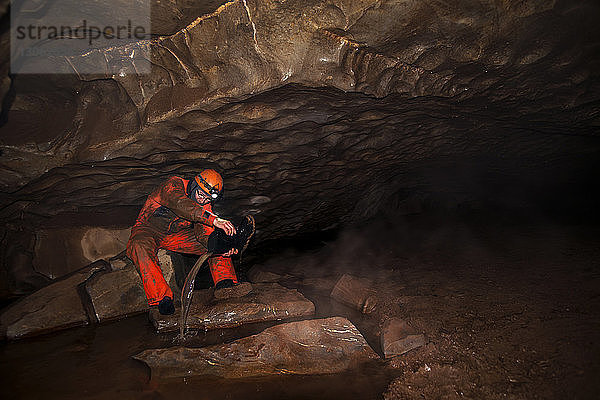 Arbeiter  der Wasser aus dem Stiefel entfernt  während er in einer Höhle sitzt
