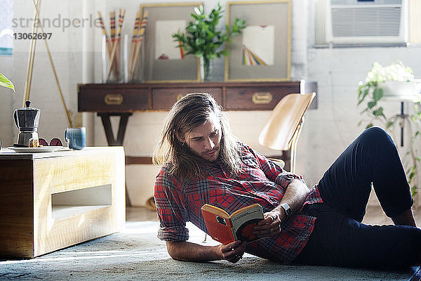 Mann liest Buch  während er zu Hause auf dem Boden liegt