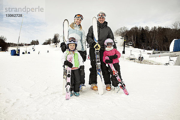 Porträt einer glücklichen Familie  die Skier auf einem schneebedeckten Feld gegen den Himmel hält
