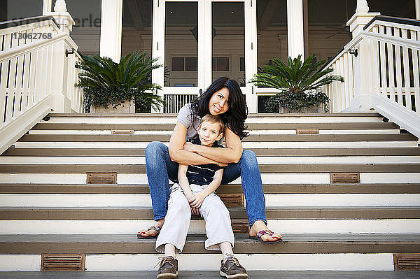 Porträt einer glücklichen Mutter  die ihren Sohn umarmt  während sie auf einer Treppe sitzt